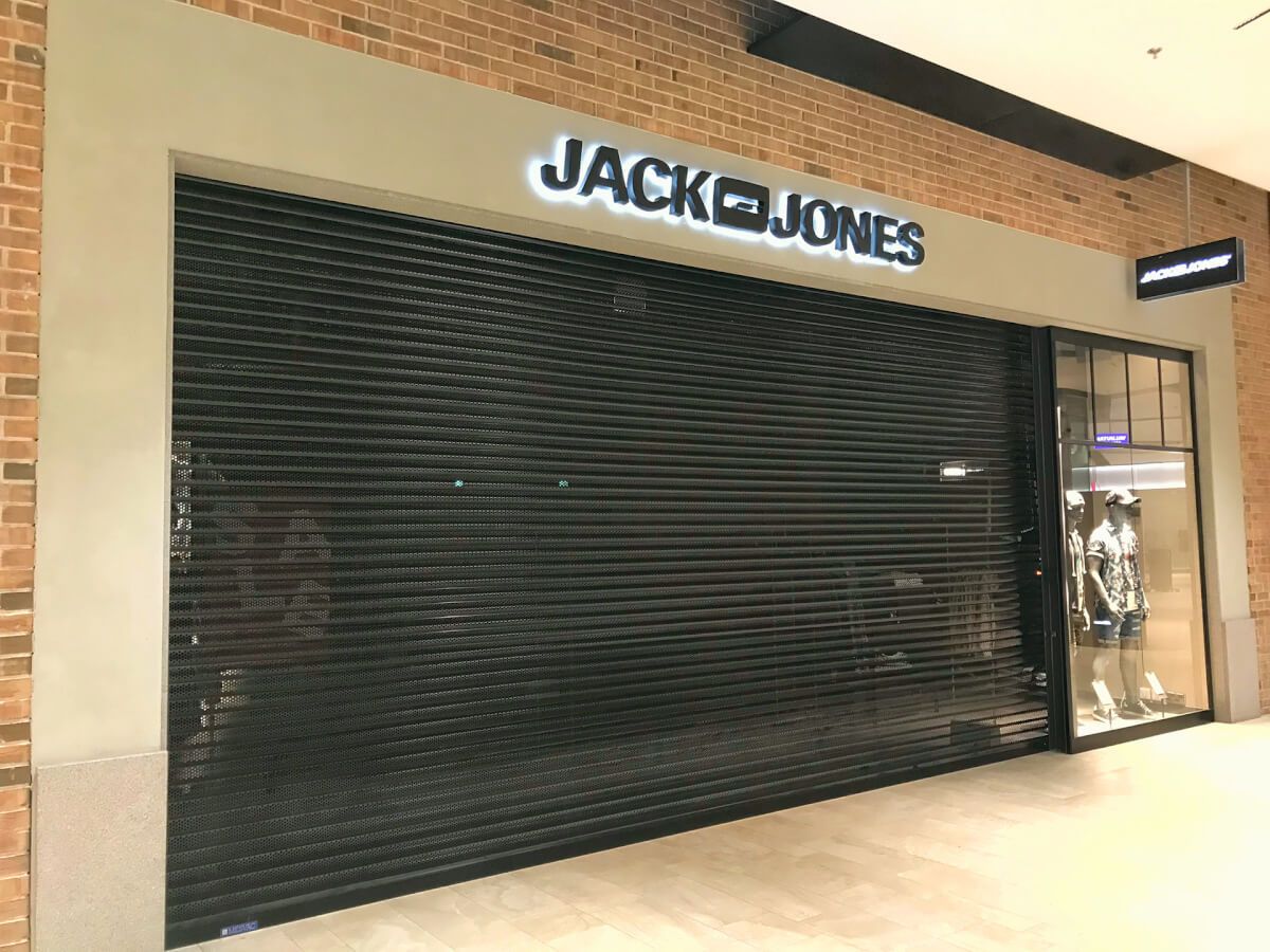 Perforated security roller shutter closed over a Jack & Jones shopfront in a shopping centre
