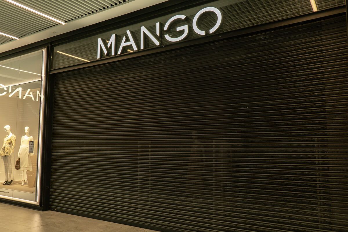 Perforated vision shutter closed over a Mango shopfront, keeping the display visible