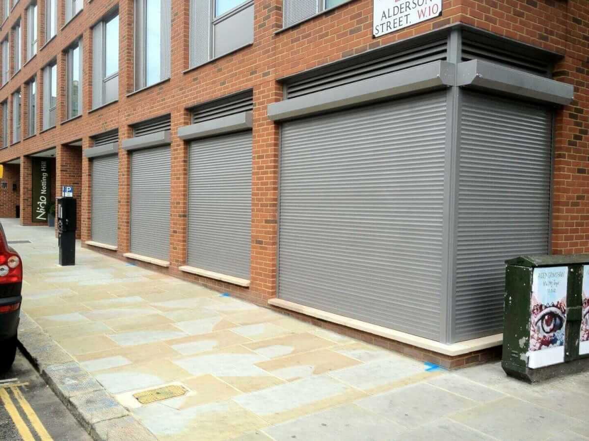 Grey security roller shutters closed over ground-floor retail units on a London street